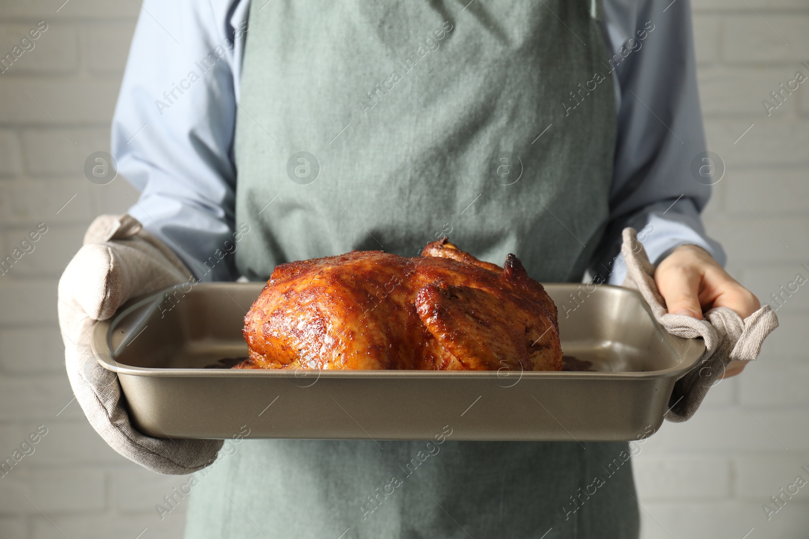 Photo of Woman holding baking tray with delicious baked turkey indoors, closeup