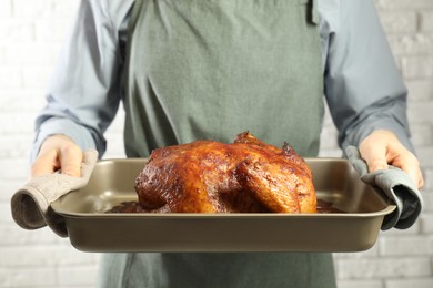 Photo of Woman holding baking tray with delicious baked turkey indoors, closeup