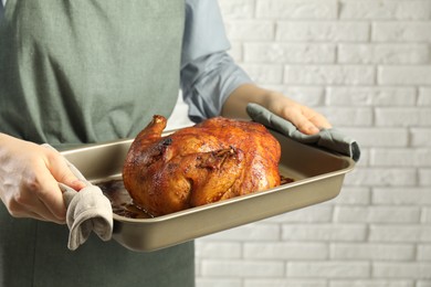 Photo of Woman holding baking tray with delicious baked turkey indoors, closeup