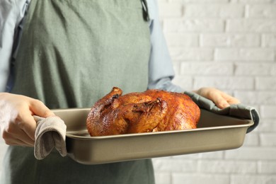 Photo of Woman holding baking tray with delicious baked turkey indoors, closeup