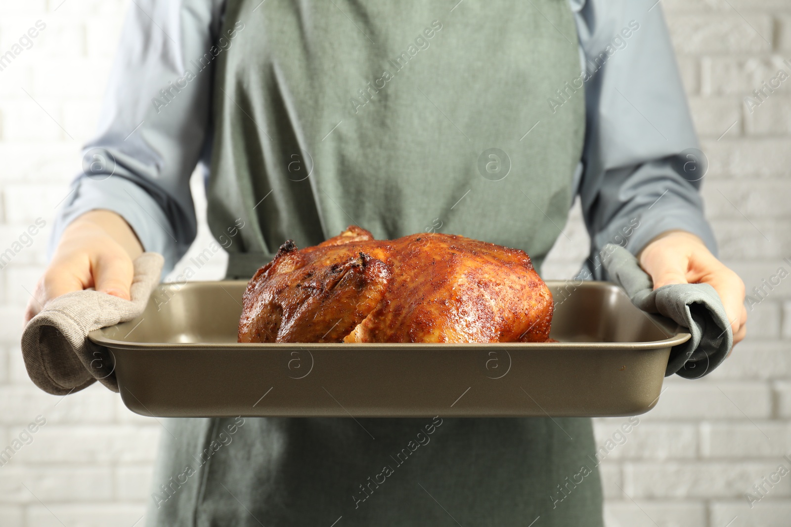 Photo of Woman holding baking tray with delicious baked turkey indoors, closeup