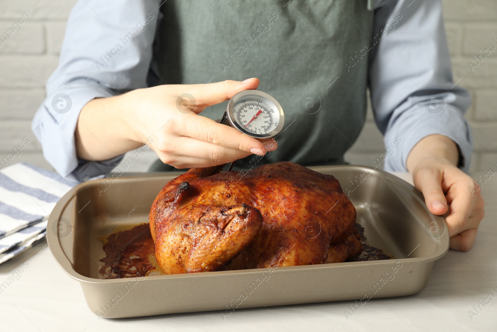 Photo of Woman measuring temperature of delicious baked turkey at light table indoors, closeup