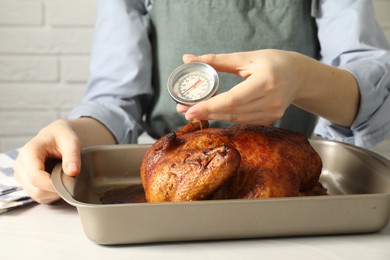 Photo of Woman measuring temperature of delicious baked turkey at light table indoors, closeup