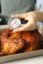 Photo of Woman measuring temperature of delicious baked turkey at light table indoors, closeup