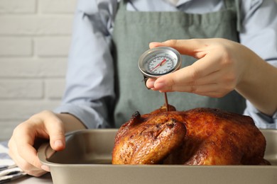 Photo of Woman measuring temperature of delicious baked turkey at table indoors, closeup