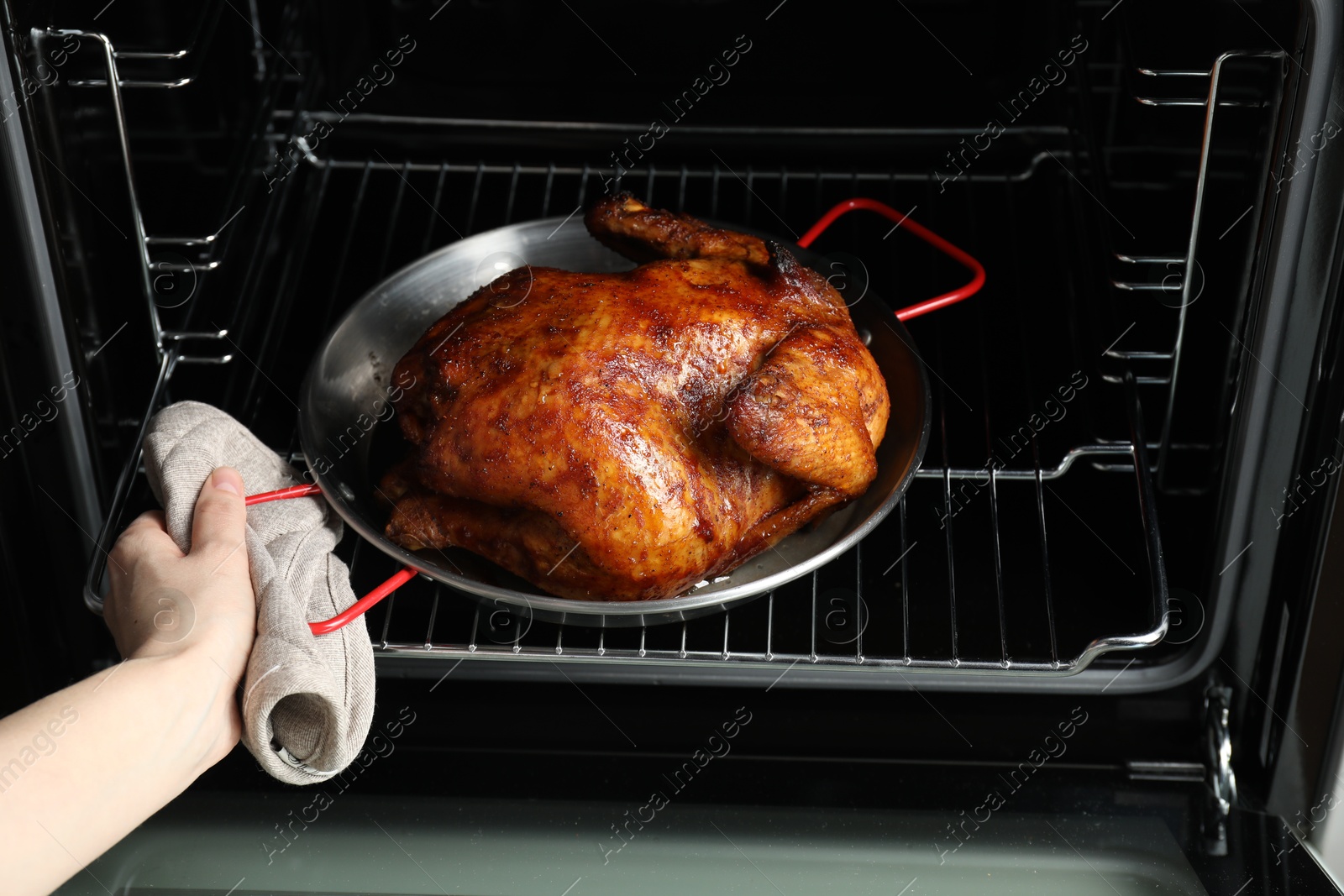 Photo of Woman taking out delicious baked turkey from oven, closeup