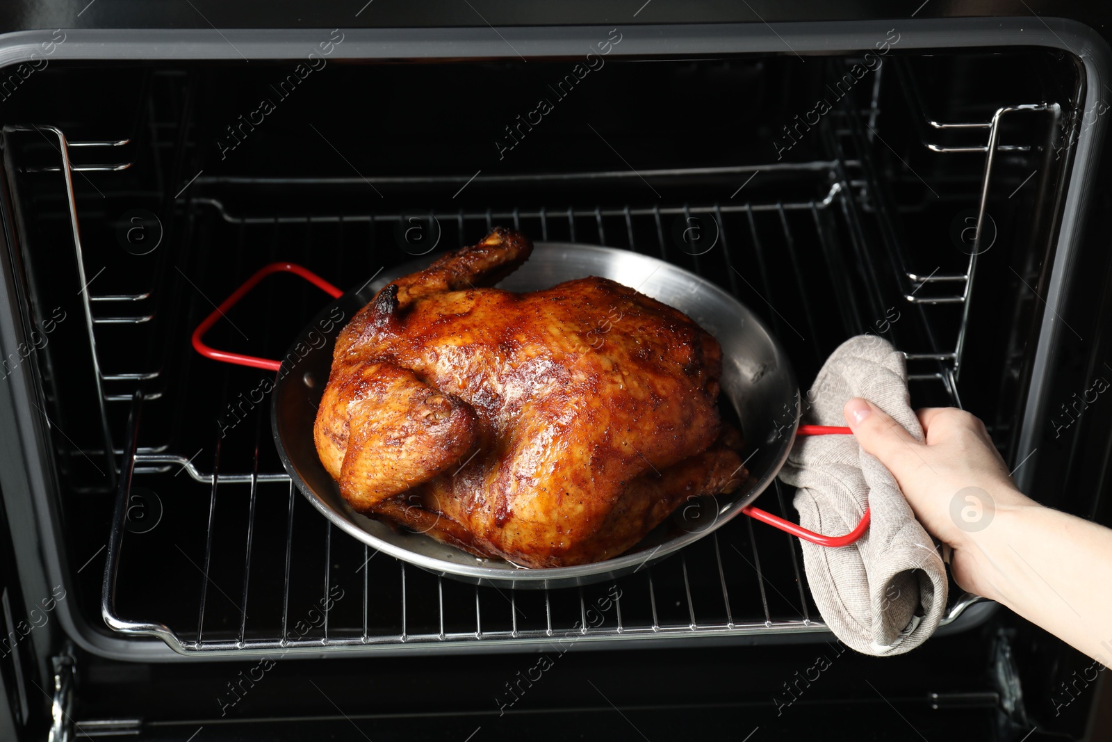 Photo of Woman taking out delicious baked turkey from oven, closeup