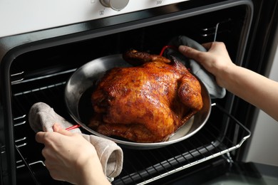 Photo of Woman taking out delicious baked turkey from oven, closeup