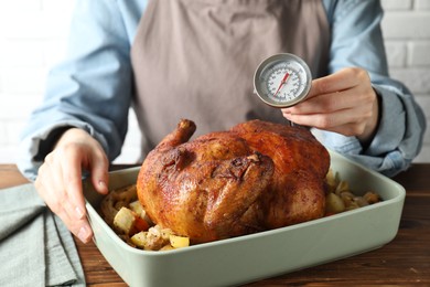 Photo of Woman measuring temperature of delicious baked turkey at wooden table indoors, closeup