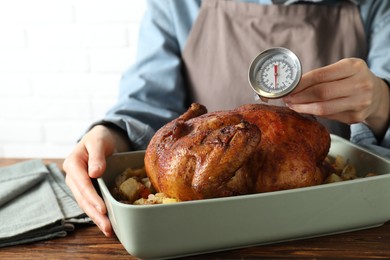 Photo of Woman measuring temperature of delicious baked turkey at wooden table indoors, closeup