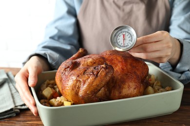 Photo of Woman measuring temperature of delicious baked turkey at wooden table indoors, closeup