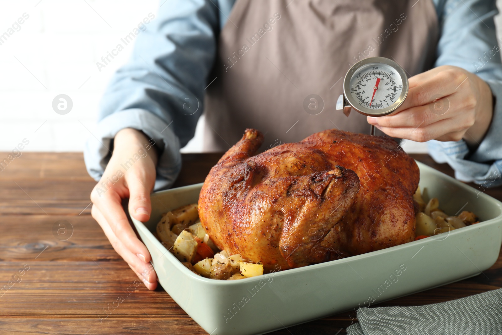 Photo of Woman measuring temperature of delicious baked turkey at wooden table indoors, closeup