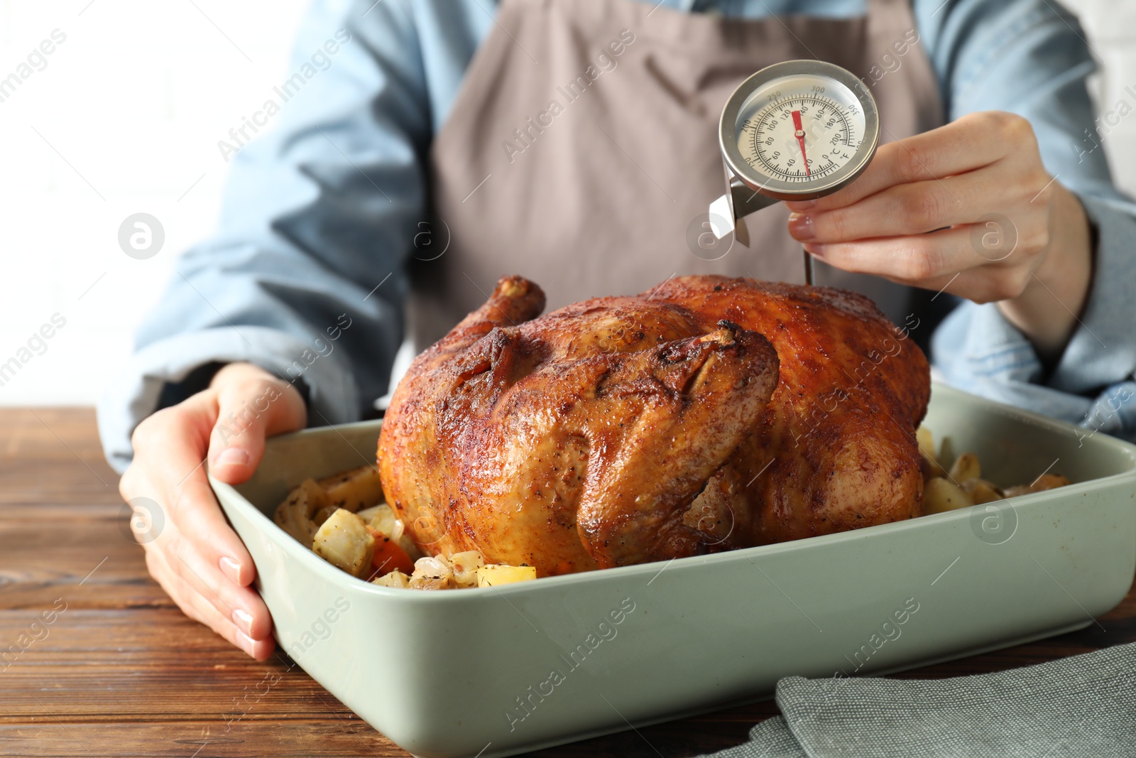 Photo of Woman measuring temperature of delicious baked turkey at wooden table indoors, closeup