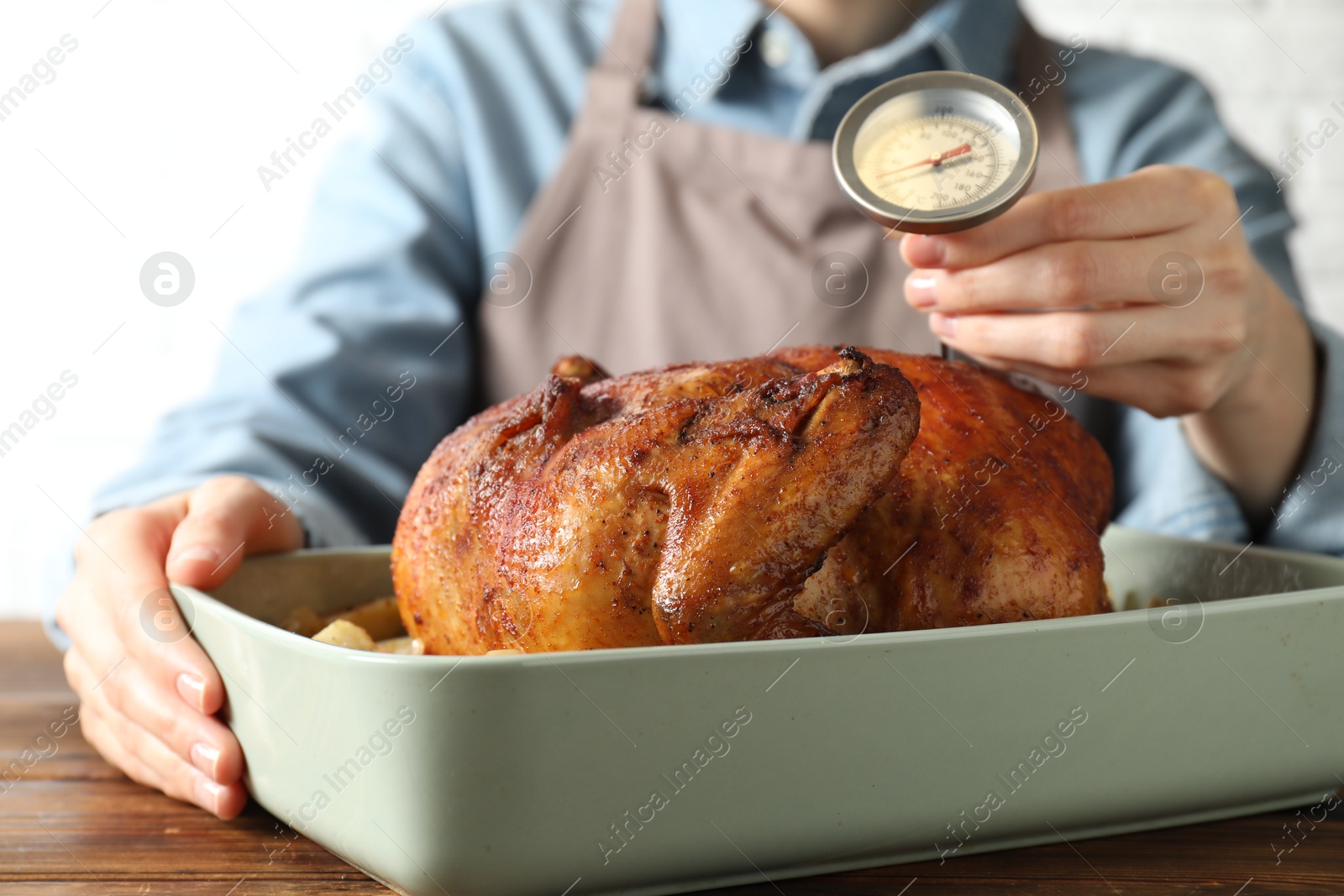 Photo of Woman measuring temperature of delicious baked turkey at wooden table indoors, closeup