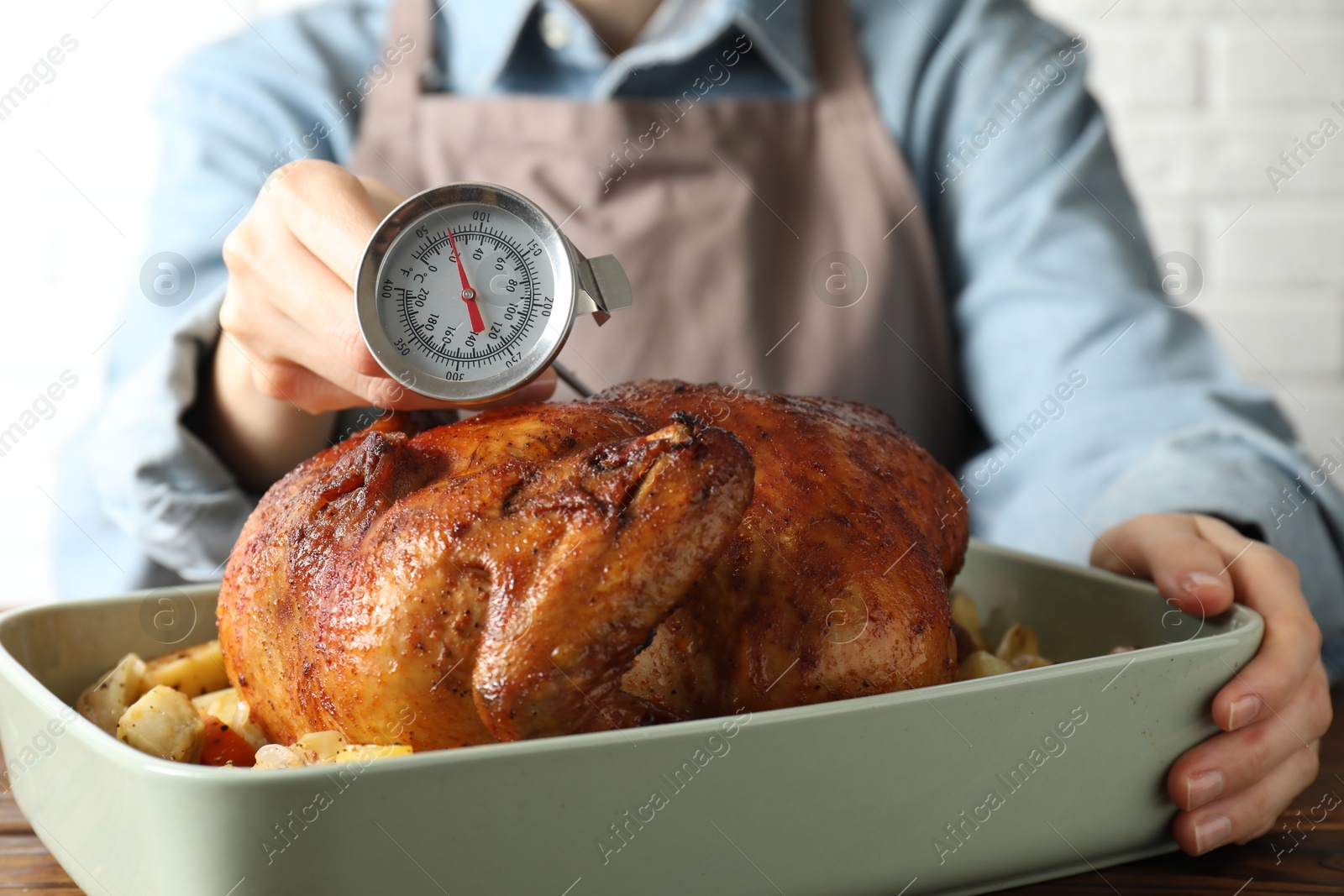 Photo of Woman measuring temperature of delicious baked turkey at table indoors, closeup