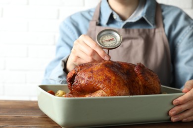 Photo of Woman measuring temperature of delicious baked turkey at wooden table indoors, closeup