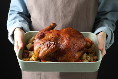 Photo of Woman holding baking tray with delicious baked turkey and vegetables on black background, closeup