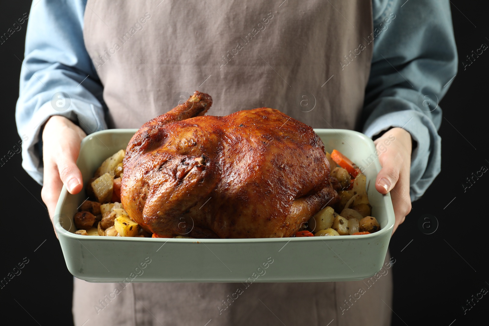 Photo of Woman holding baking tray with delicious baked turkey and vegetables on black background, closeup