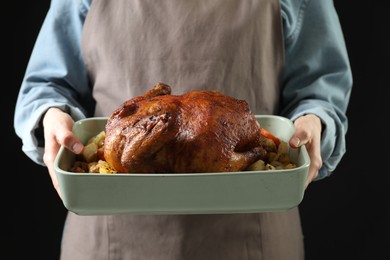 Photo of Woman holding baking tray with delicious baked turkey and vegetables on black background, closeup