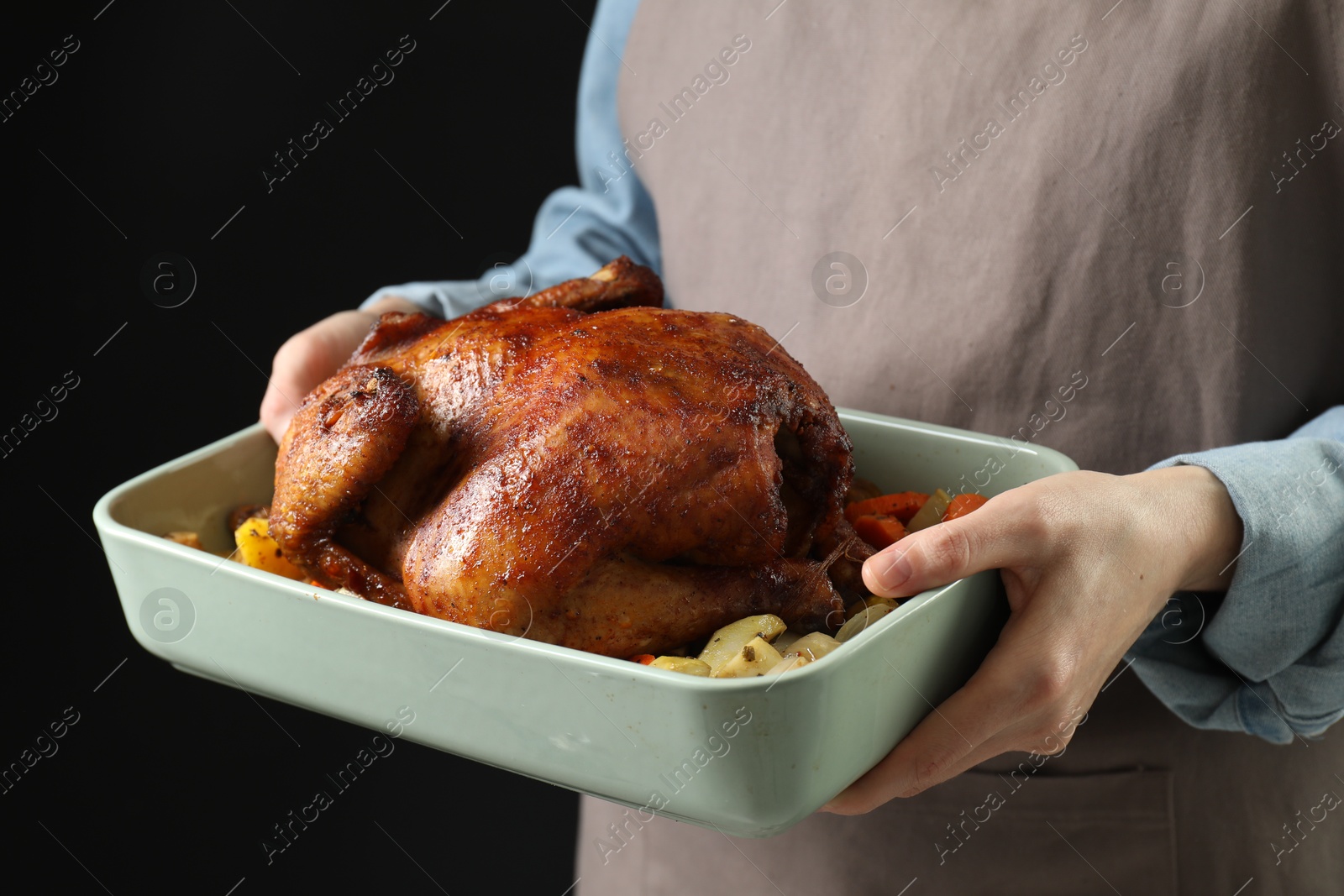 Photo of Woman holding baking tray with delicious baked turkey and vegetables on black background, closeup