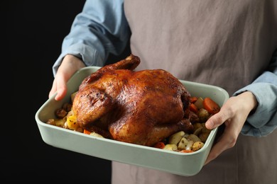 Photo of Woman holding baking tray with delicious baked turkey and vegetables on black background, closeup