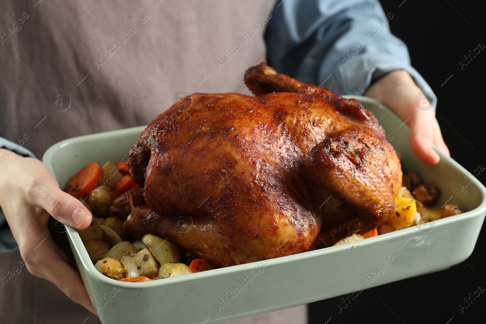 Photo of Woman holding baking tray with delicious baked turkey and vegetables on black background, closeup