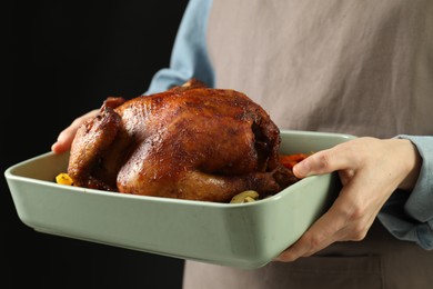 Photo of Woman holding baking tray with delicious baked turkey and vegetables on black background, closeup