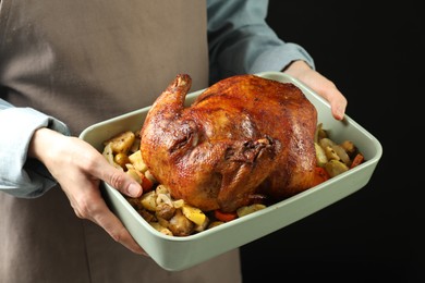 Photo of Woman holding baking tray with delicious baked turkey and vegetables on black background, closeup