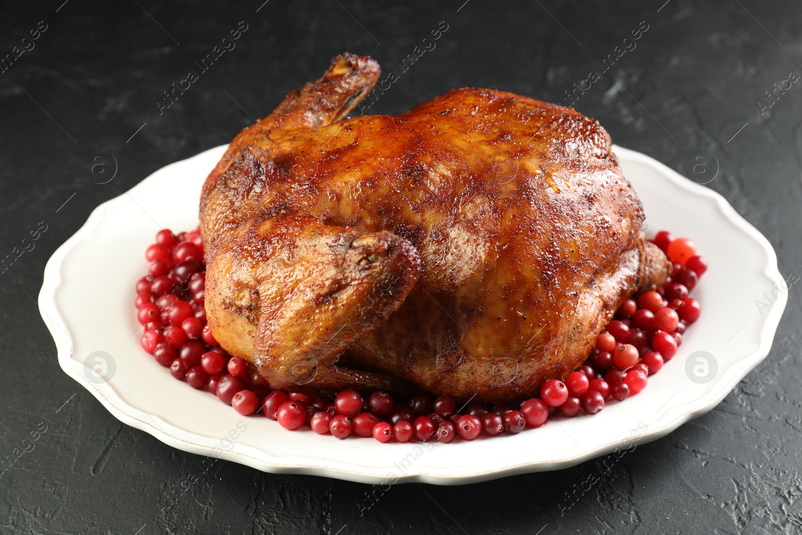 Photo of Delicious baked turkey and cranberries on dark gray textured table, closeup