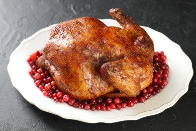 Photo of Delicious baked turkey and cranberries on dark gray textured table, closeup