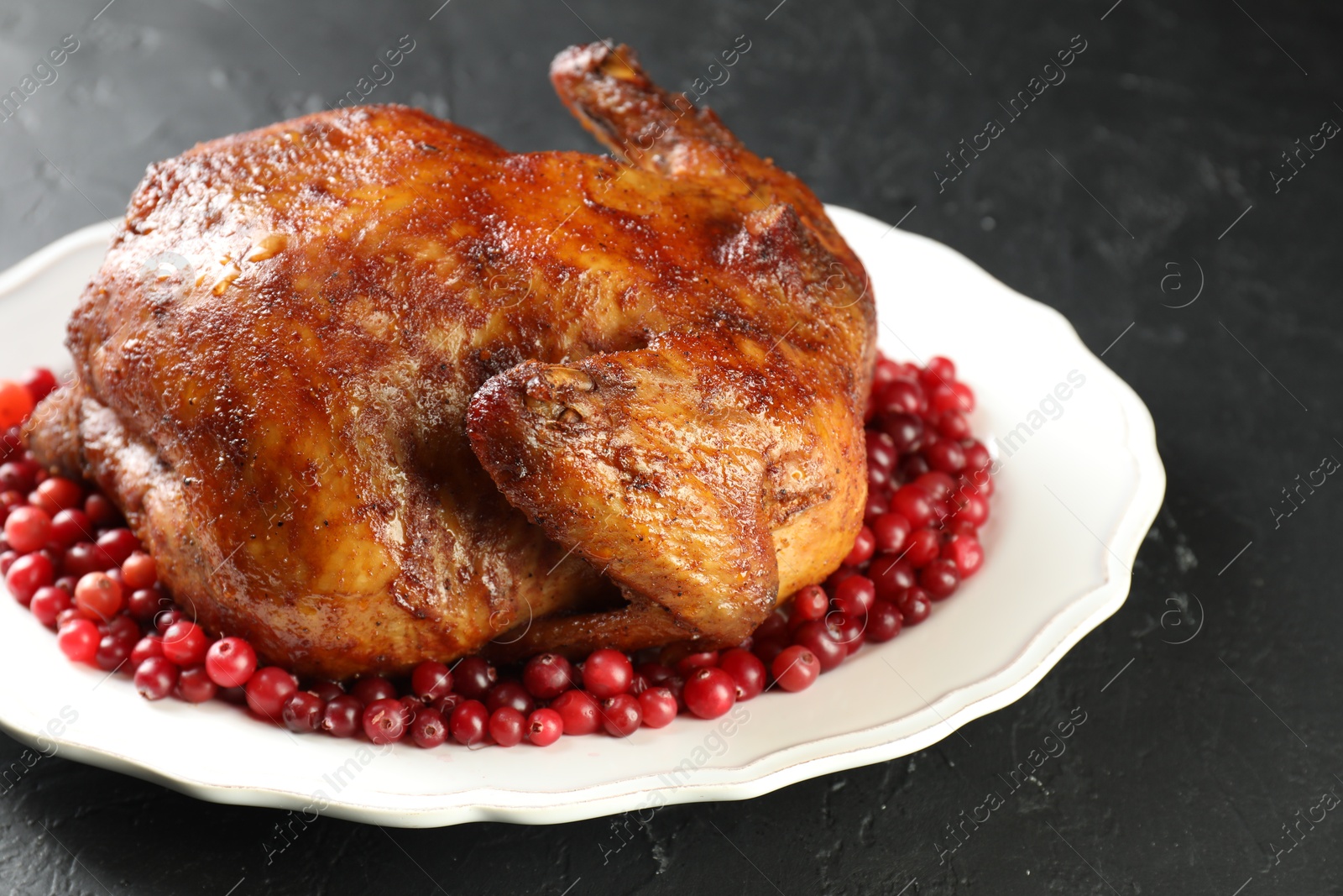 Photo of Delicious baked turkey and cranberries on dark gray textured table, closeup