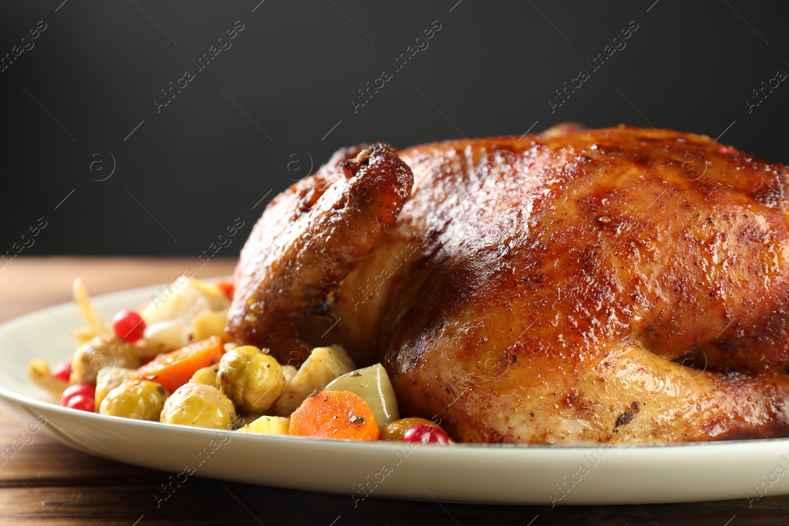 Photo of Delicious baked turkey, vegetables and cranberries on wooden table against gray background, closeup