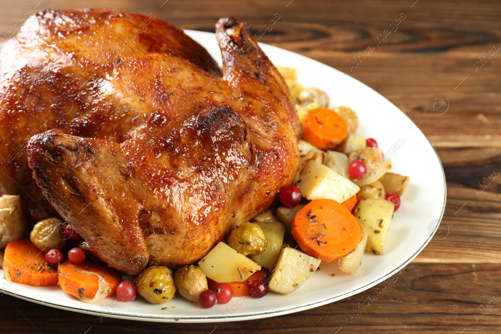 Photo of Delicious baked turkey, vegetables and cranberries on wooden table, closeup