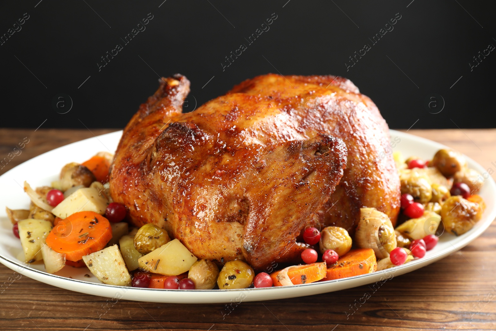 Photo of Delicious baked turkey, vegetables and cranberries on wooden table against gray background, closeup