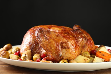 Photo of Delicious baked turkey, vegetables and cranberries on wooden table against black background, closeup