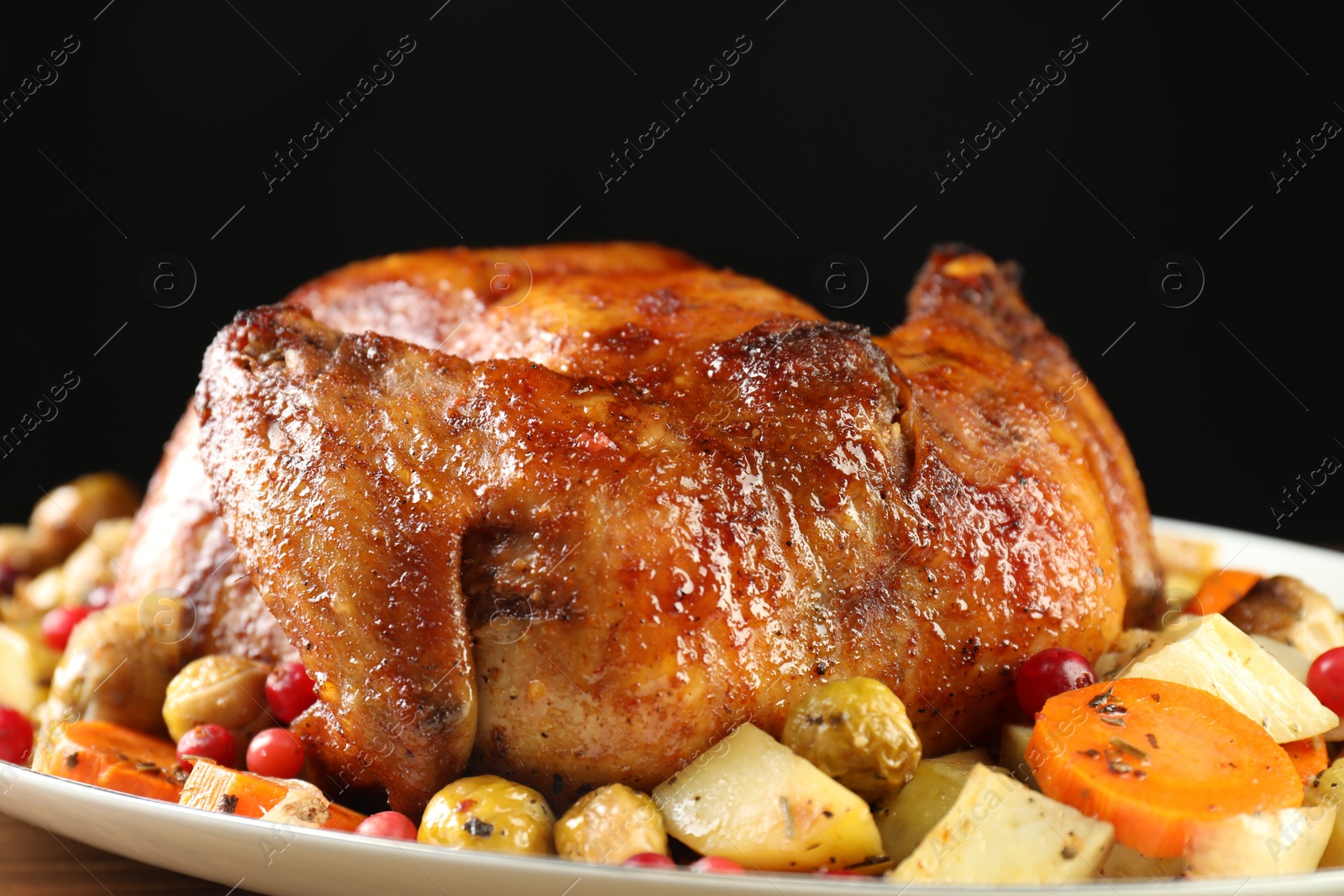 Photo of Delicious baked turkey, vegetables and cranberries on table against black background, closeup