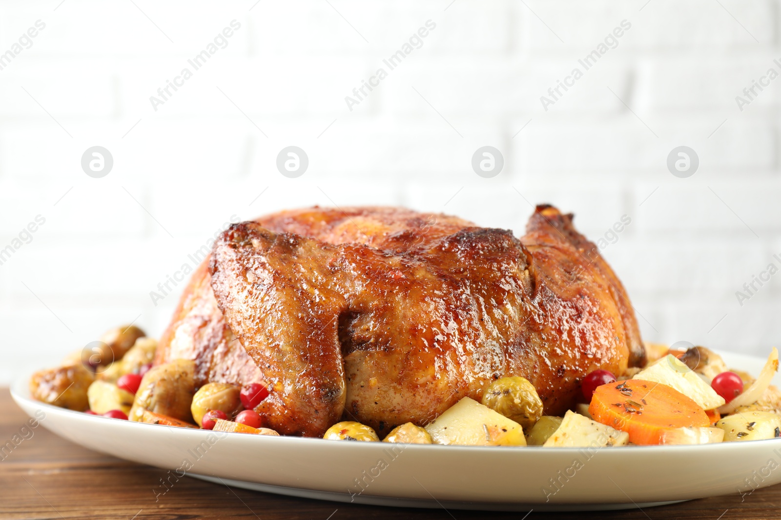 Photo of Delicious baked turkey, vegetables and cranberries on wooden table against white brick wall, closeup