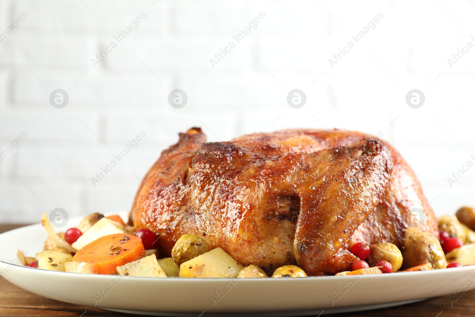 Photo of Delicious baked turkey, vegetables and cranberries on wooden table against white brick wall, closeup