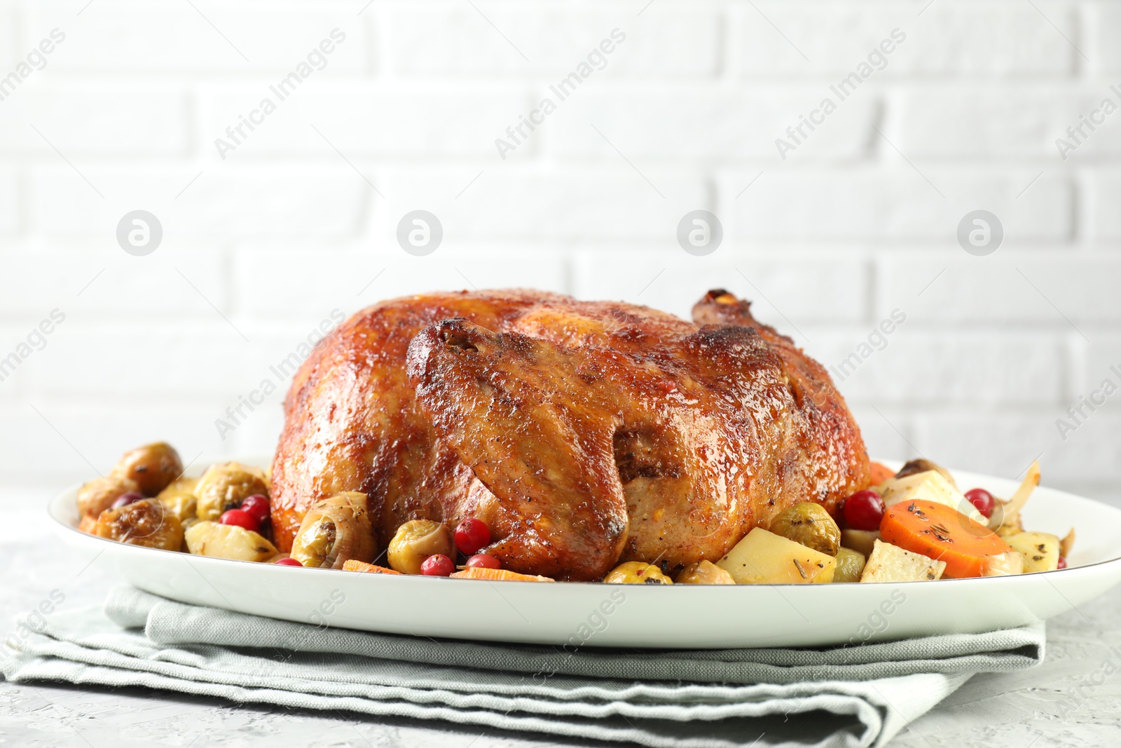 Photo of Delicious baked turkey, vegetables and cranberries on gray textured table against white brick wall closeup