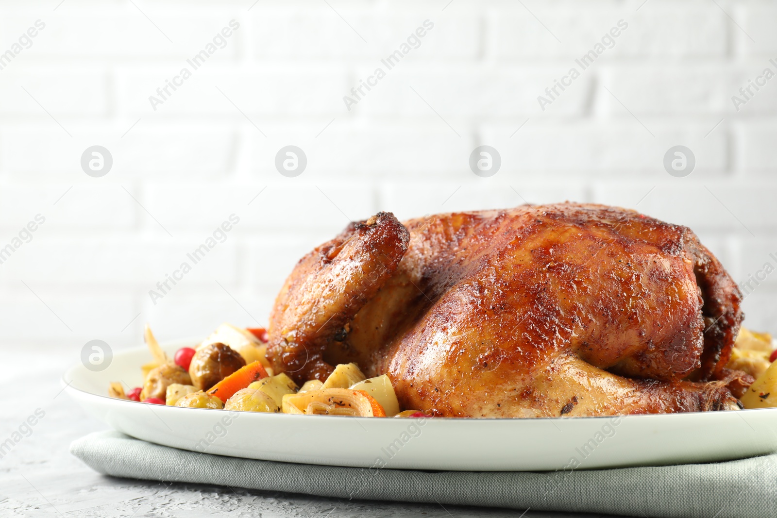 Photo of Delicious baked turkey and vegetables on gray textured table against white brick wall, space for text