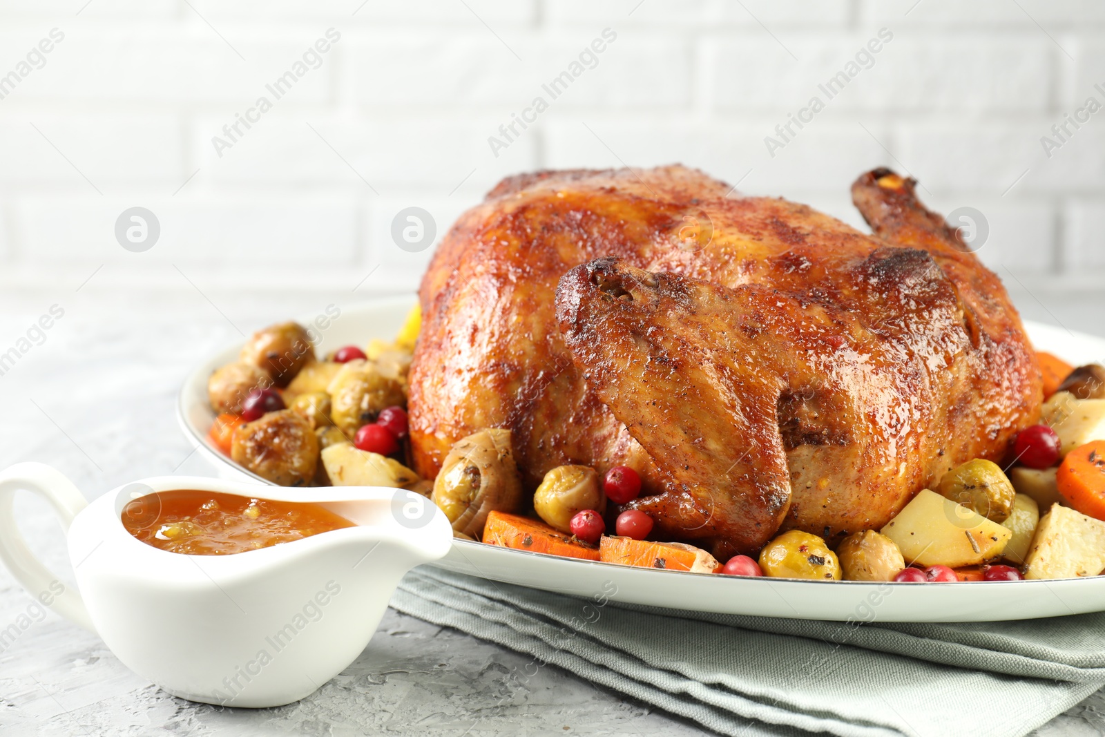 Photo of Delicious baked turkey, vegetables, cranberries and orange sauce on gray textured table indoors