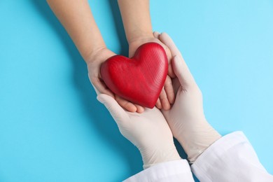 Photo of Doctor and child holding heart model on light blue background, top view