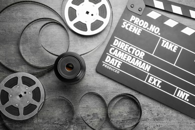 Photo of Flat lay composition with movie clapper, film reels and camera lens on grey textured table