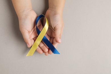 Photo of Child with yellow and blue ribbon on dark beige background, top view. Down syndrome awareness