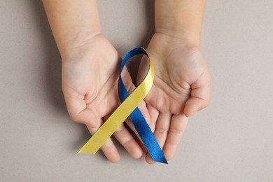 Photo of Child with yellow and blue ribbon on dark beige background, top view. Down syndrome awareness