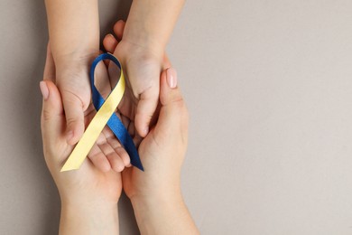 Photo of Woman with child holding yellow and blue ribbon on dark beige background, top view. Down syndrome awareness