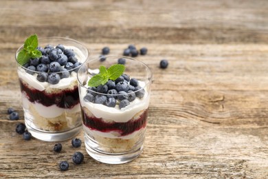 Photo of Tasty trifle dessert. Sponge cake, blueberries, jam and whipped cream in glasses on wooden table, closeup. Space for text