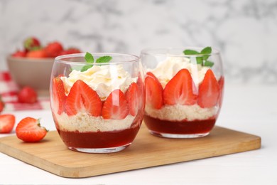 Photo of Tasty trifle dessert. Sponge cake, strawberries, jam and whipped cream in glasses on white table, closeup