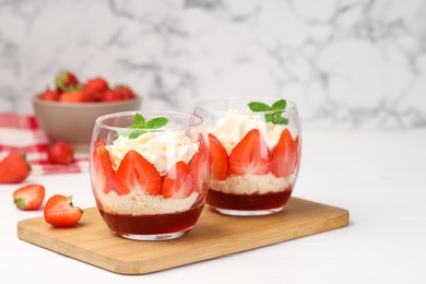 Photo of Tasty trifle dessert. Sponge cake, strawberries, jam and whipped cream in glasses on white table