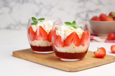 Photo of Tasty trifle dessert. Sponge cake, strawberries, jam and whipped cream in glasses on white table, closeup